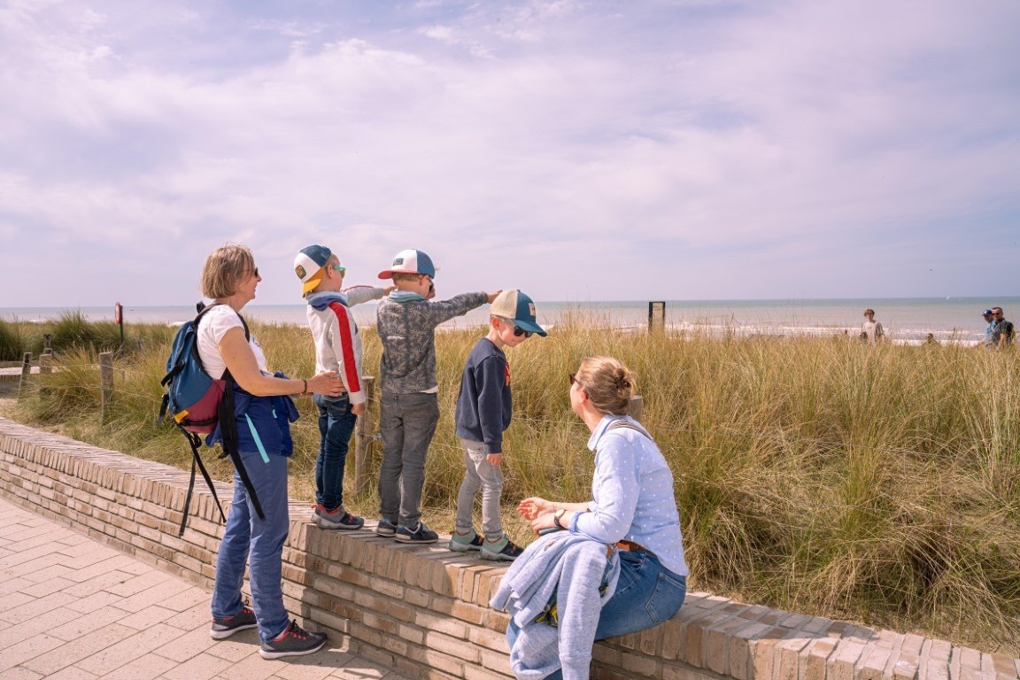 Gezin op de zeedijk van Westende kijkt over de duinen naar zee
